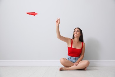 Photo of Beautiful young woman playing with paper plane near light grey wall