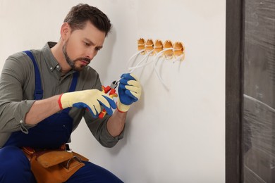 Electrician in uniform with pliers repairing power socket indoors