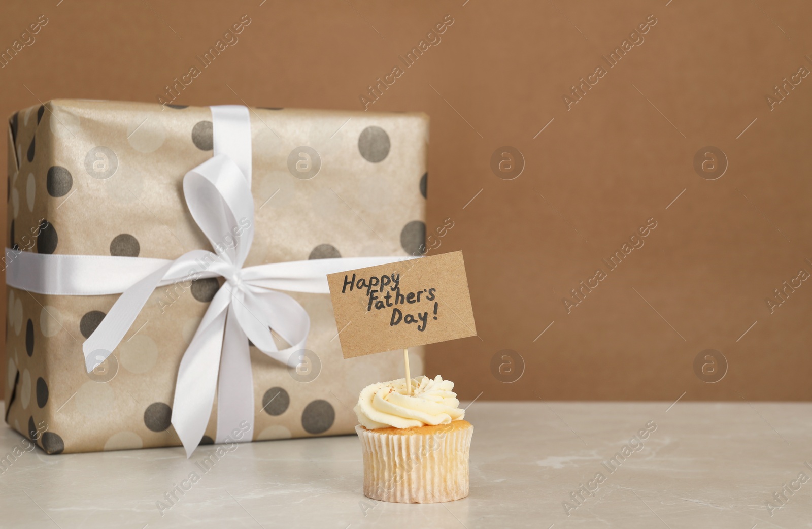 Photo of Happy Father's Day. Tasty cupcake with greetings and gift box on light marble table. Space for text