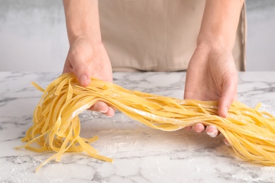 Photo of Woman holding raw egg noodles over marble table, closeup