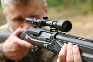 Photo of Man aiming with hunting rifle outdoors, selective focus