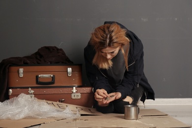 Photo of Poor homeless woman with suitcase counting coins on floor near dark wall