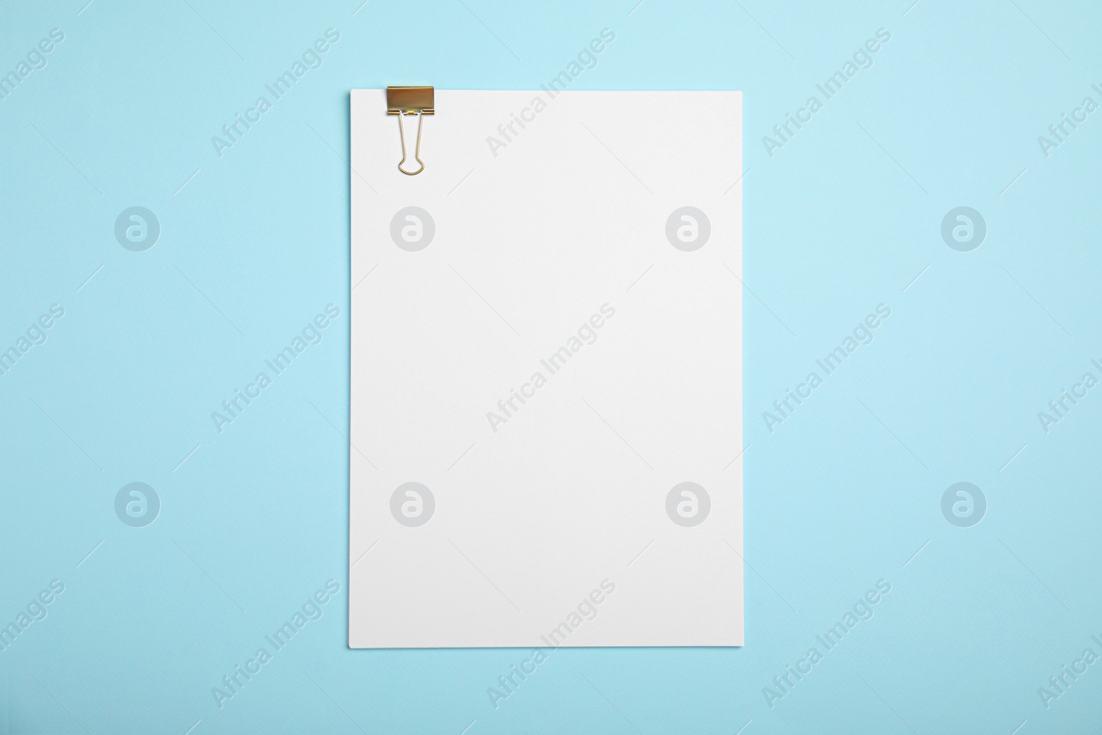 Photo of Sheet of paper with clip on light blue background, top view