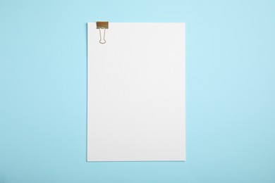 Sheet of paper with clip on light blue background, top view