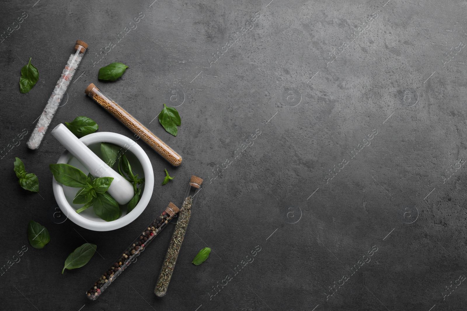 Photo of Test tubes with different spices, fresh basil leaves, mortar and pestle on grey background, flat lay. Space for text