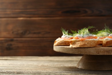 Photo of Tasty canapes with salmon, cucumber, cream cheese and dill on wooden table, space for text