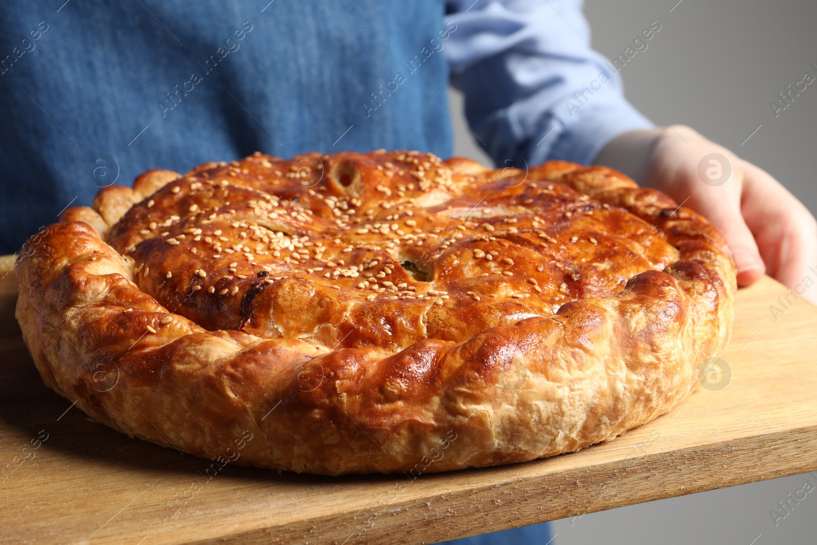 Photo of Woman holding tasty homemade pie on light grey background, closeup