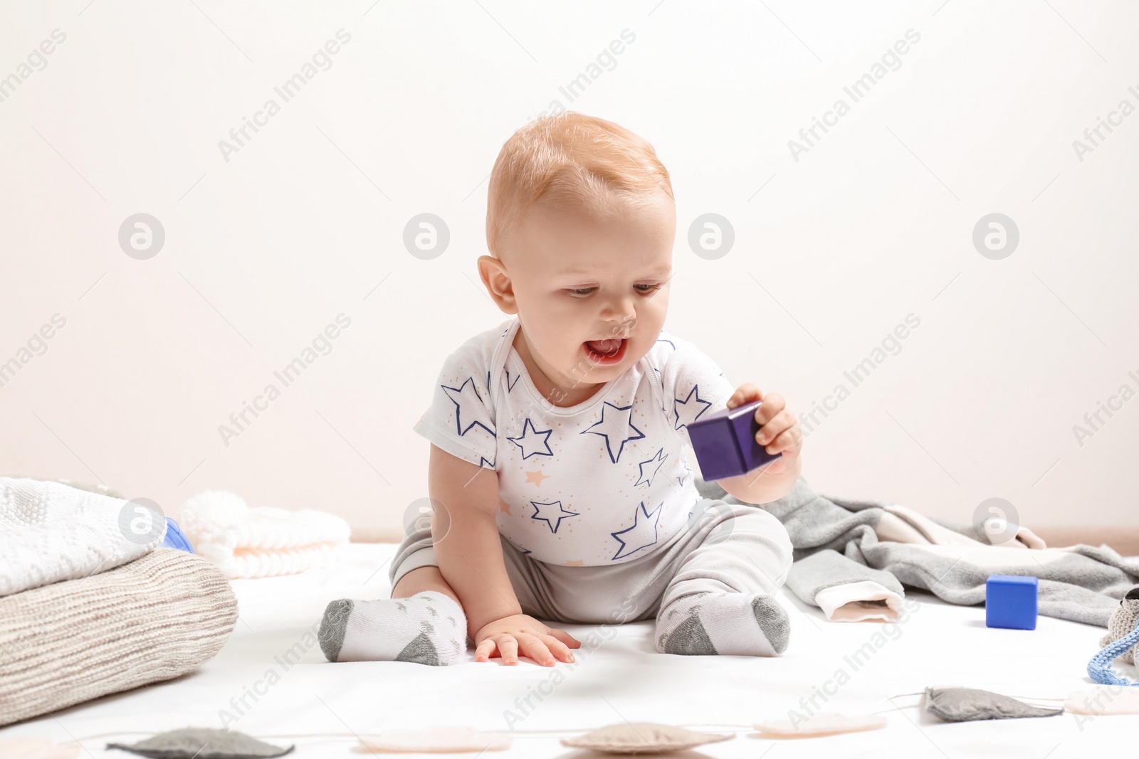 Photo of Little boy in cute clothes sitting on floor against light background. Baby accessories