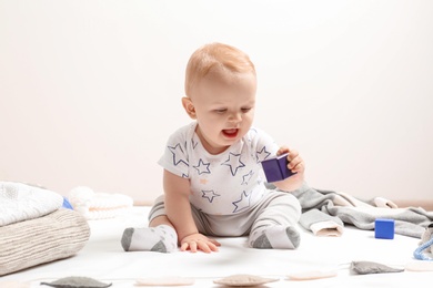 Photo of Little boy in cute clothes sitting on floor against light background. Baby accessories