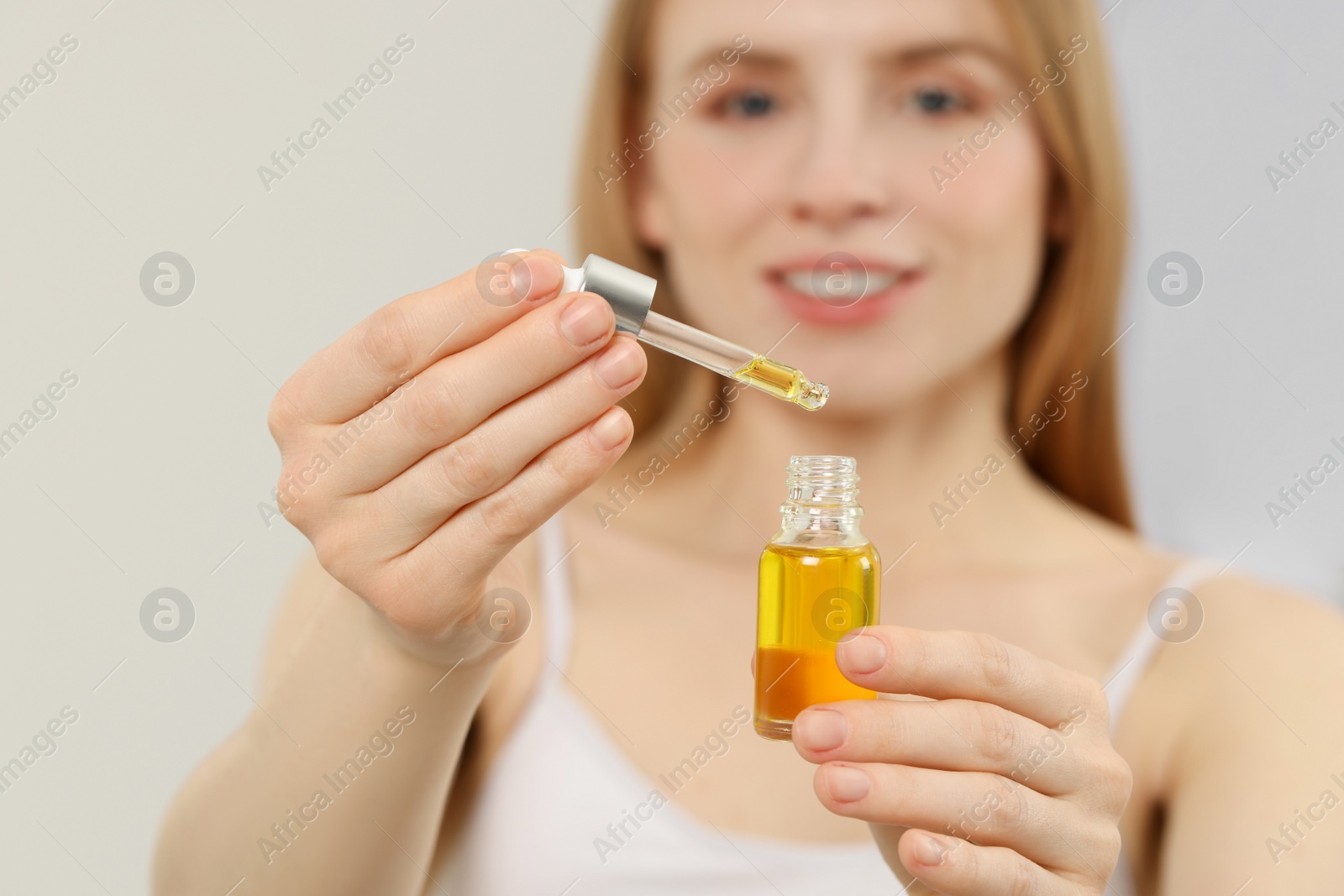 Photo of Woman with bottle of essential oil on blurred background, selective focus