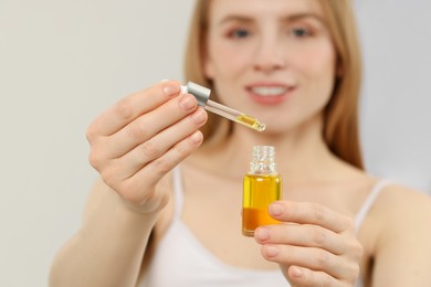 Photo of Woman with bottle of essential oil on blurred background, selective focus