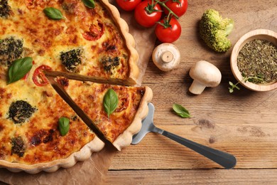 Photo of Taking piece of delicious homemade vegetable quiche and ingredients on wooden table, flat lay