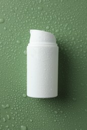 Moisturizing cream in bottle on green background with water drops, top view