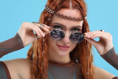 Photo of Stylish young hippie woman in sunglasses on light blue background, closeup