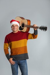 Photo of Man in Santa hat with acoustic guitar on light grey background. Christmas music
