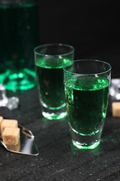 Photo of Absinthe in shot glasses, spoon and brown sugar cubes on gray table, closeup. Alcoholic drink