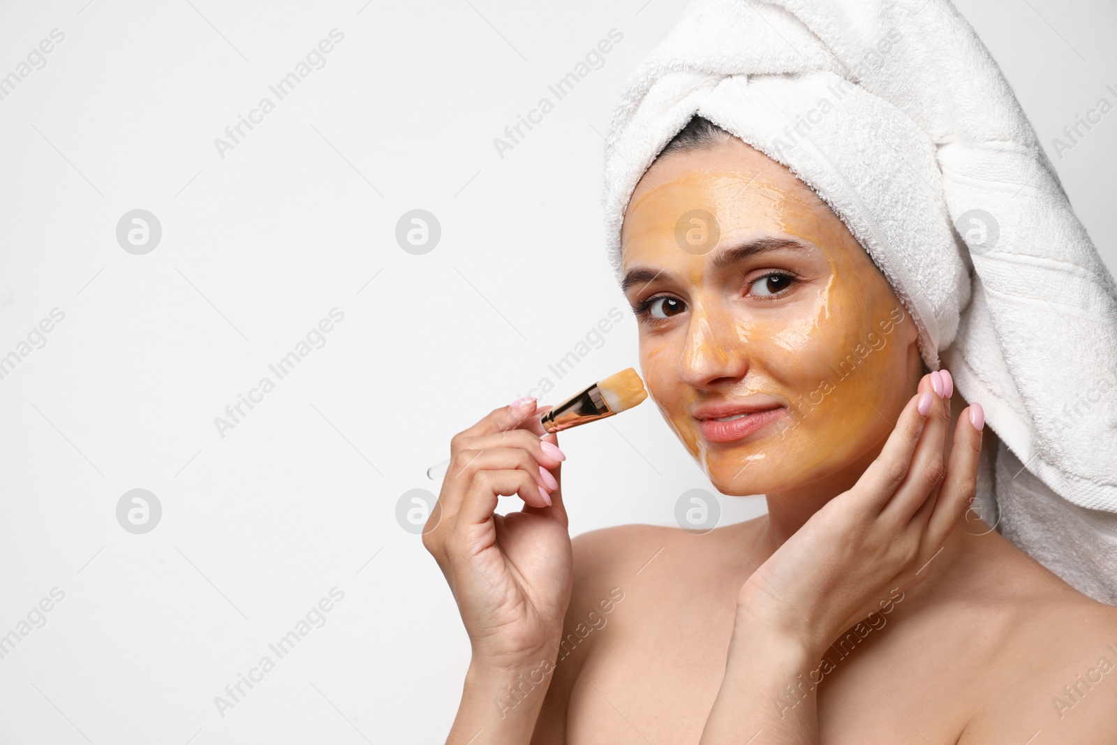 Photo of Beautiful woman applying mask onto face against light background. Space for text