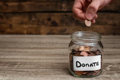 Photo of Man putting coin into donation jar on table, closeup. Space for text