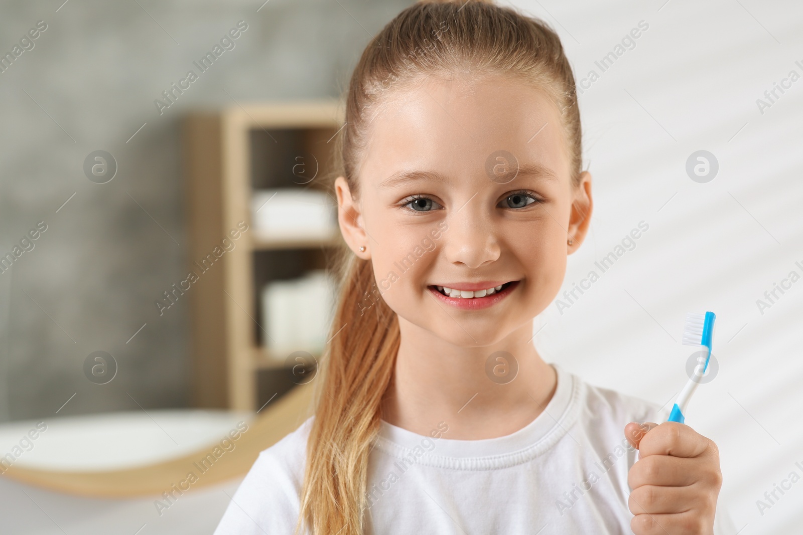 Photo of Cute little girl holding plastic toothbrush in bathroom, space for text