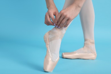 Young ballerina tying pointe shoes on light blue background, closeup
