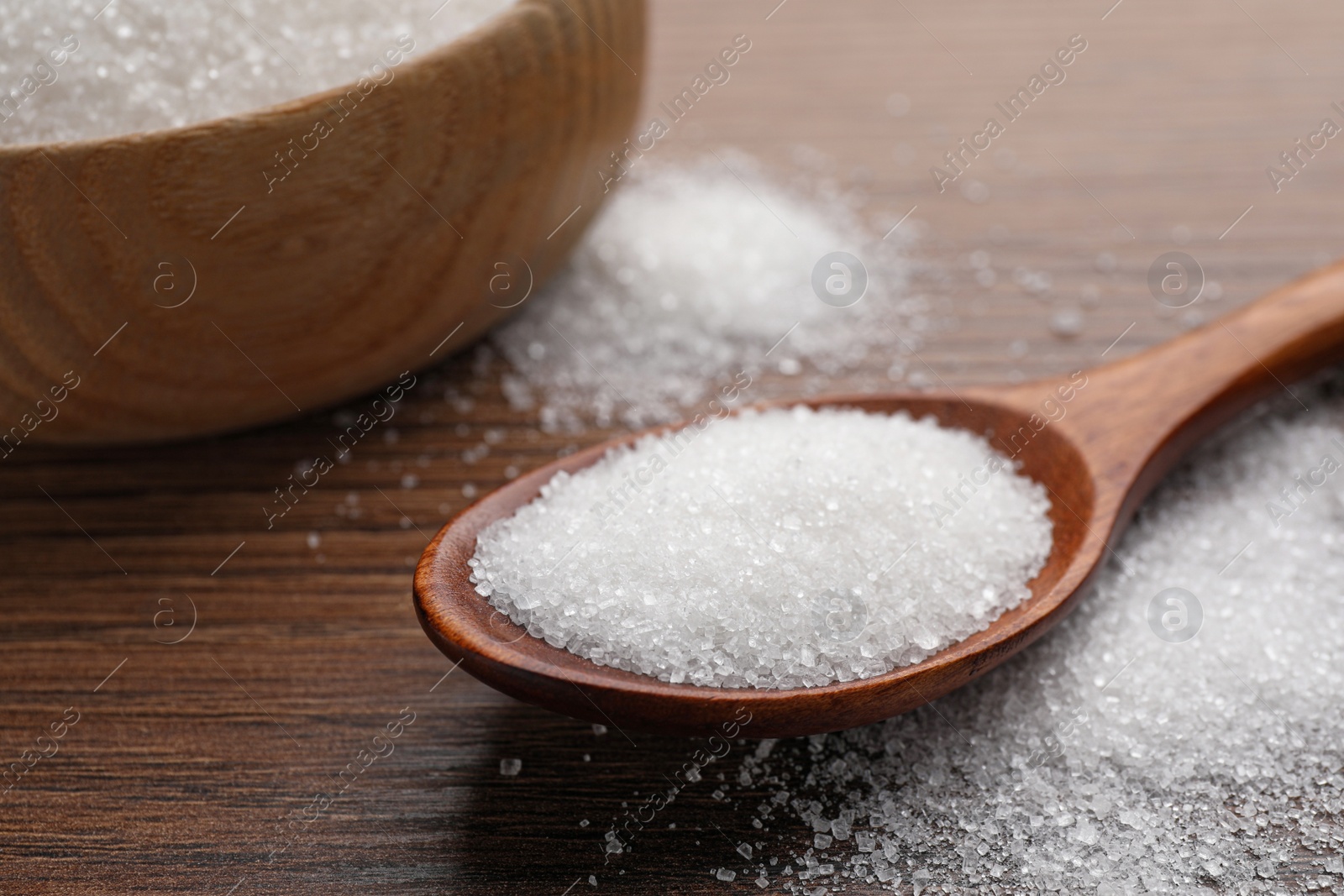 Photo of Granulated sugar on wooden table, closeup view