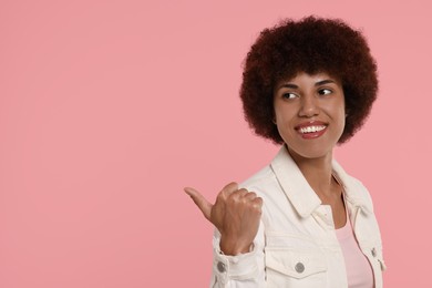 Happy young woman pointing at something on pink background. Space for text