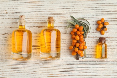 Photo of Natural sea buckthorn oil and fresh berries on white wooden table, flat lay