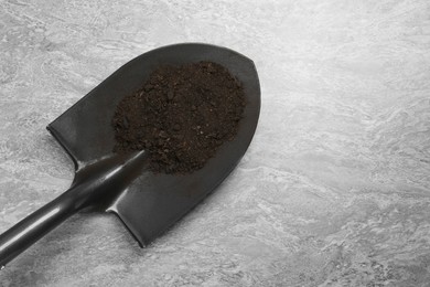 Photo of Metal shovel with fertile soil on gray textured surface, top view. Space for text