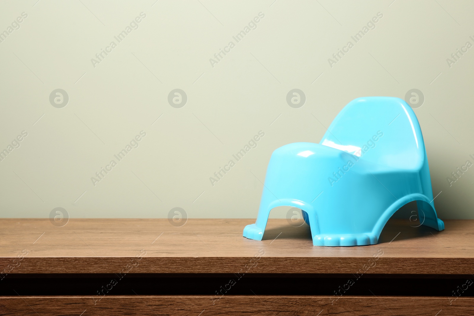 Photo of Light blue baby potty on wooden table against olive background, space for text. Toilet training