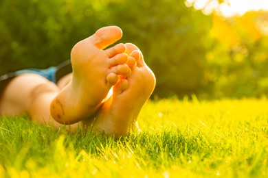 Photo of Teenage girl lying barefoot on green grass outdoors, closeup. Space for text