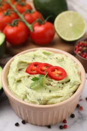 Bowl of delicious guacamole and ingredients on white table, closeup