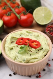 Photo of Bowl of delicious guacamole and ingredients on white table, closeup