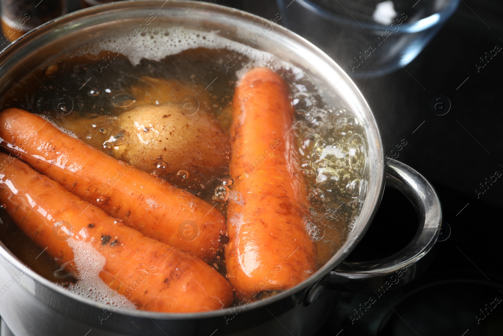 Photo of Boiling carrot and potatoes in pot on electric stove, closeup. Cooking vinaigrette salad