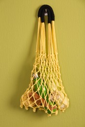 Photo of Conscious consumption. Net bag with eco friendly products hanging on olive wall