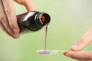 Woman pouring cough syrup into dosing spoon on light green background, closeup