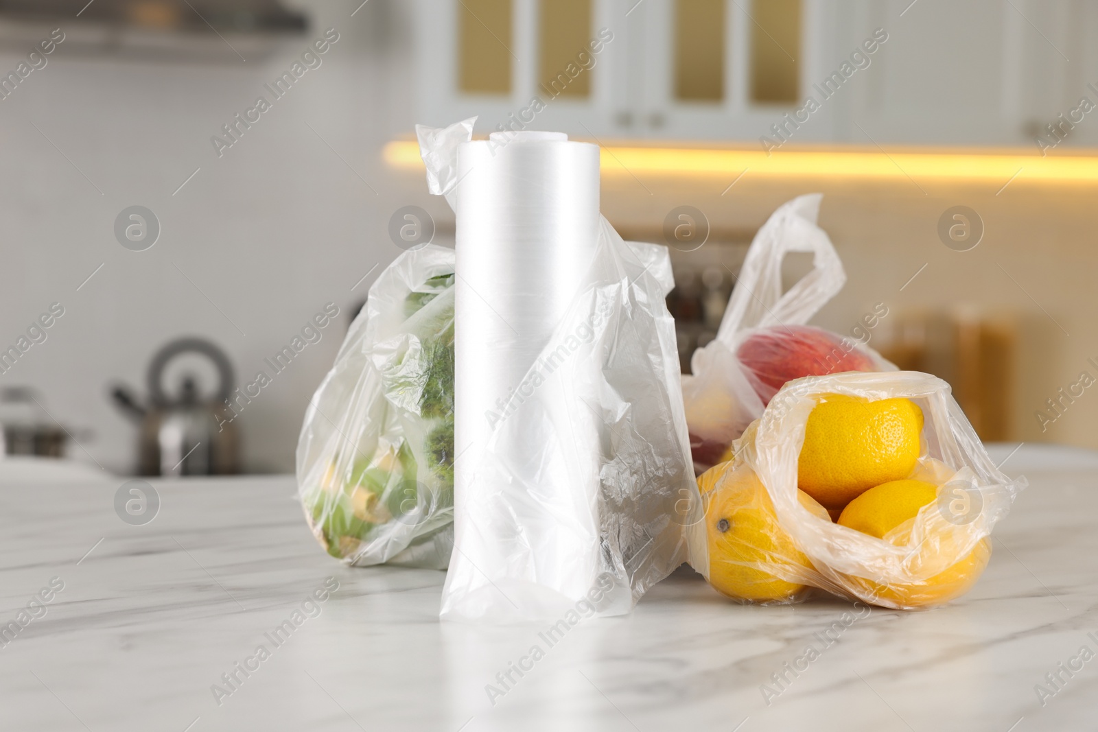 Photo of Plastic bags with different fresh products on white marble table in kitchen