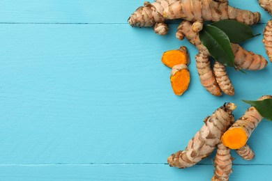 Photo of Whole and cut turmeric roots on light blue wooden table, flat lay. Space for text