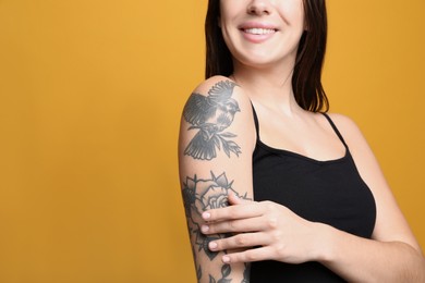 Photo of Beautiful woman with tattoos on arm against yellow background, closeup. Space for text
