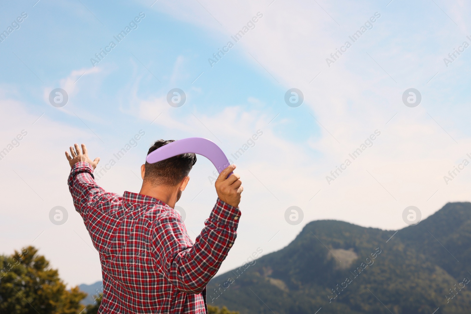 Photo of Man throwing boomerang in mountains on sunny day, back view. Space for text