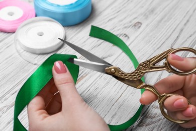 Photo of Woman cutting green ribbon with scissors at white wooden table, closeup