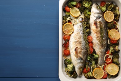 Photo of Delicious fish with vegetables and lemon in baking dish on blue wooden table, top view. Space for text