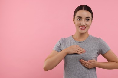 Beautiful young woman doing breast self-examination on pink background, space for text