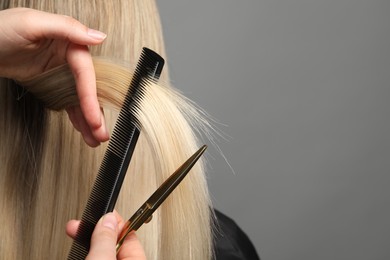 Hairdresser combing and cutting client's hair on light grey background, closeup. Space for text