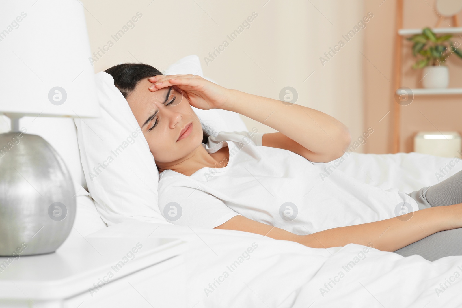 Photo of Young woman suffering from headache on bed at home. Hormonal disorders