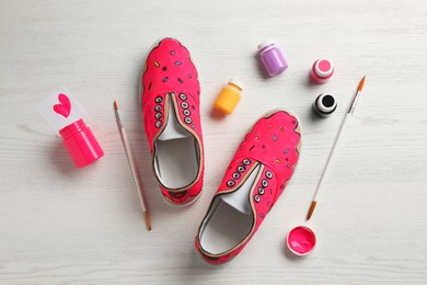Photo of Amazing customized shoes and painting supplies on white wooden background, flat lay