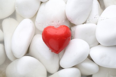 Red decorative heart on stones and water, top view