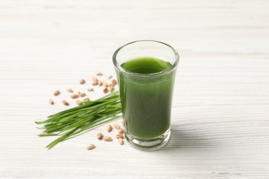 Photo of Wheat grass drink in shot glass, seeds and fresh green sprouts on white wooden table, closeup