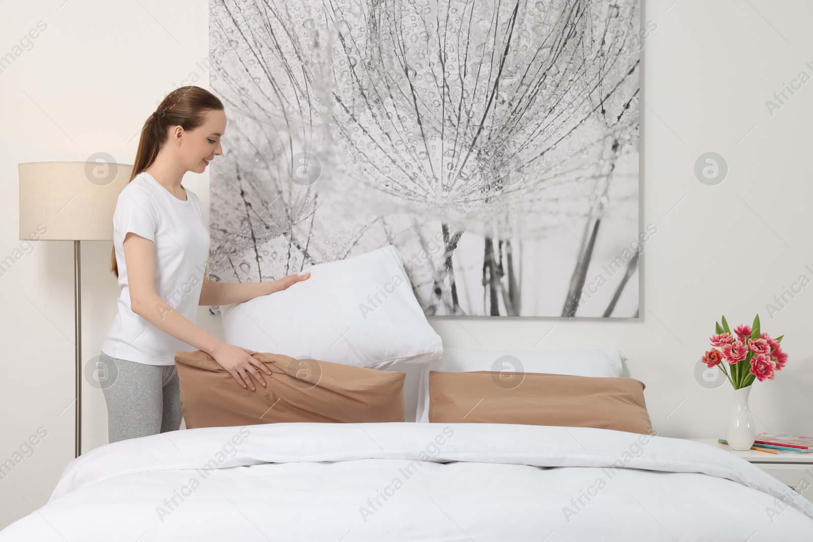 Photo of Young woman making bed in room. Space for text