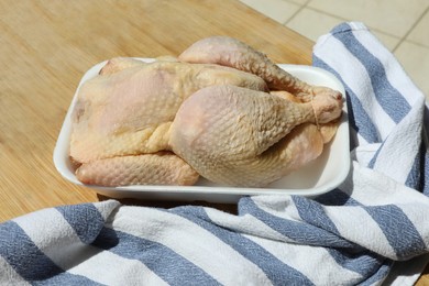 Fresh raw whole chicken in plastic container and napkin on wooden table