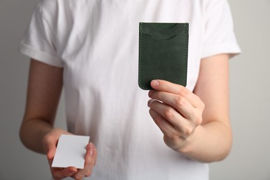 Woman holding leather business card holder and blank card on grey background, closeup